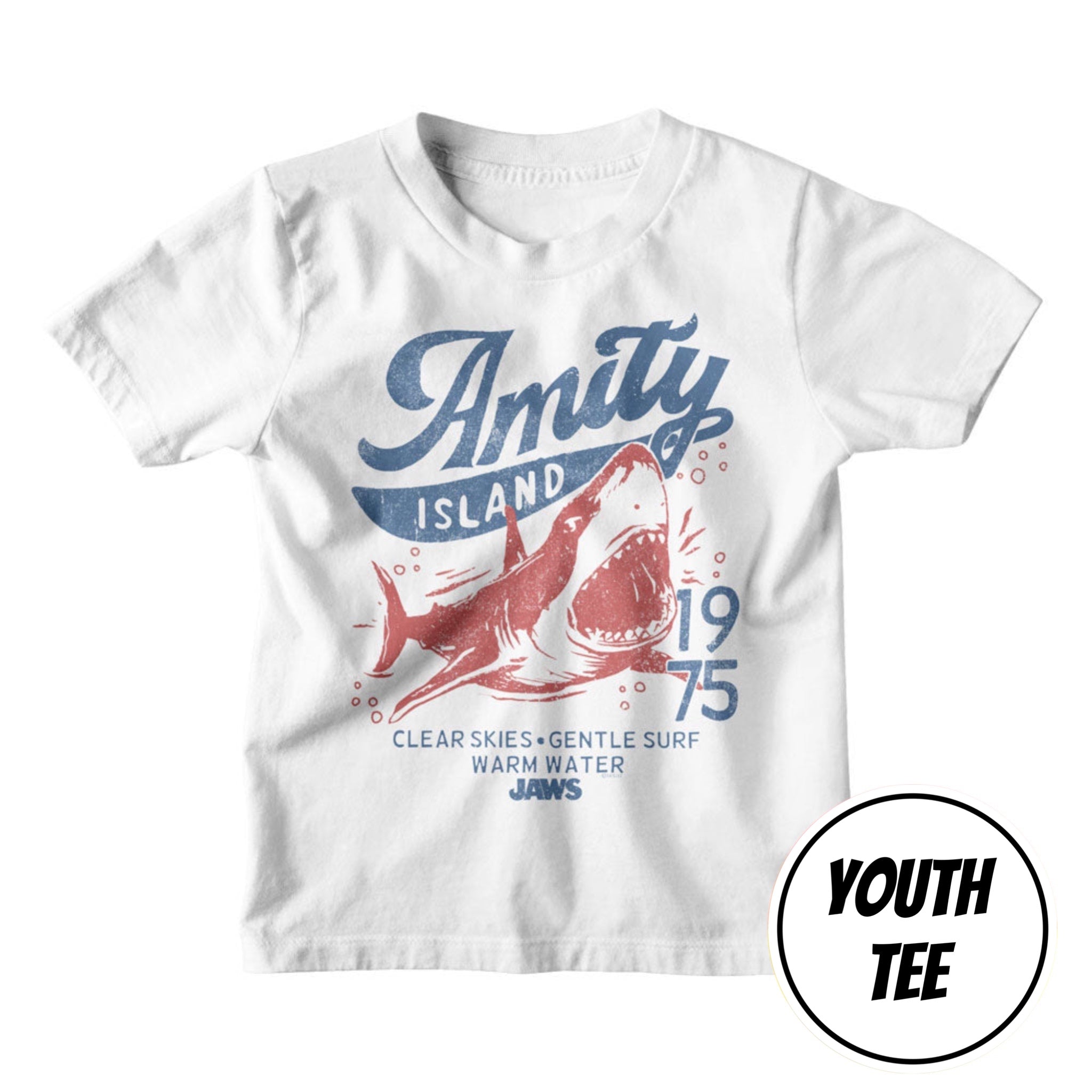 A white youth short-sleeve t-shirt with a vintage-style red and blue graphic on the front. The graphic features the text 'Amity Island 1975' and 'Clear Skies • Gentle Surf • Warm Water • Jaws' surrounding a red shark illustration.