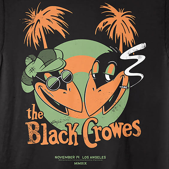 A black short-sleeve graphic t-shirt featuring a cartoon illustration of two black-crow-like birds wearing sunglasses and a green hat, with orange palm trees and the text 'the Black Crowes' on the front.