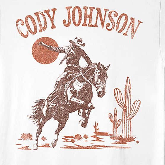 A white short-sleeve crewneck t-shirt featuring a distressed brown graphic of a cowboy riding a bucking horse under a large sun, with the text 'CODY JOHNSON' printed above.