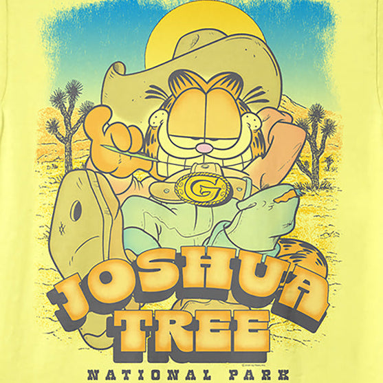 A pale yellow short-sleeve graphic T-shirt featuring Garfield as Joshua Tree National Park, with a large western-style illustration and the text 'JOSHUA TREE NATIONAL PARK' on the front.