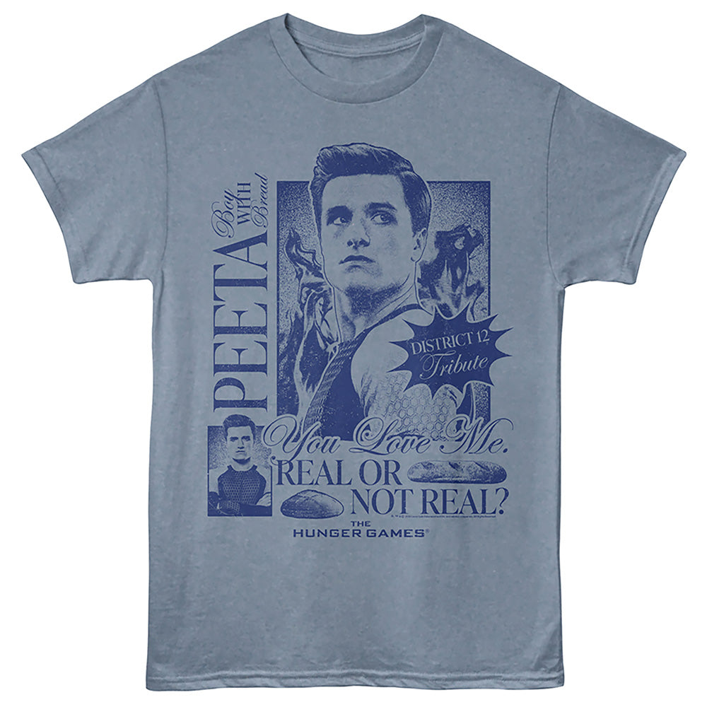 A light blue crewneck t-shirt featuring a dark blue graphic print of Peeta from Hunger Games, with text including 'PEETA', 'You Love Me. REAL OR NOT REAL?', and 'District 12 Tribute'.