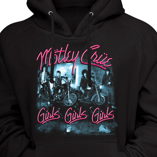 A black pullover hoodie featuring a front graphic print of the band Motley Crue with their 'Girls Girls Girls' album artwork. The text is written in a vibrant pink neon-style font, and the central graphic depicts the band members on motorcycles in a dark, moody blue-toned scene.