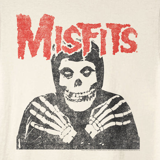An off-white crewneck t-shirt featuring a distressed black graphic of a skull in a striped hoodie with skeletal hands, and the word 'Misfits' printed in a red, textured font above it.
