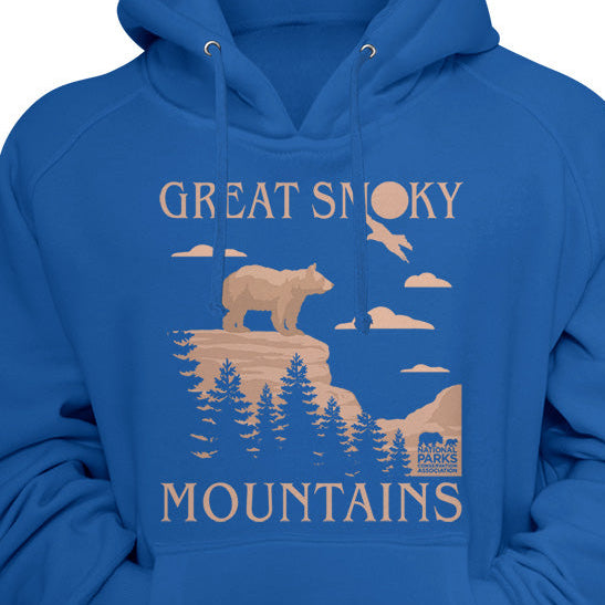A royal blue pullover hoodie with a vintage-style front graphic that reads 'GREAT SMOKY MOUNTAINS' in beige, featuring a bear, trees, mountains, and a small cabin illustration.