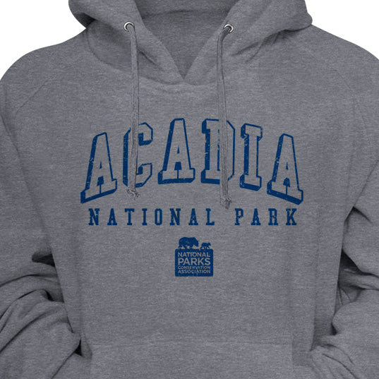 A heather gray pullover hoodie featuring a blue graphic print on the chest that reads 'ACADIA NATIONAL PARK' with a small park logo underneath, shown against a gray background.